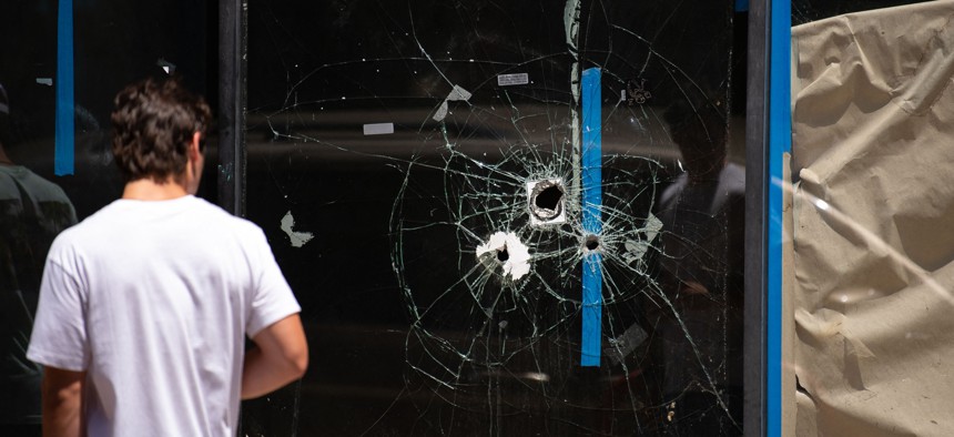 A pedestrian walks past bullet holes in the window of a storefront on South Street in Philadelphia on June 5, 2022.