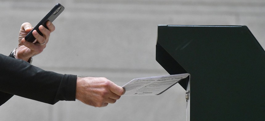 A man photographs himself depositing his ballot in an official ballot drop box while a long line of voters queue outside of Philadelphia City Hall at the satellite polling station on October 27, 2020 in Philadelphia, Pennsylvania.