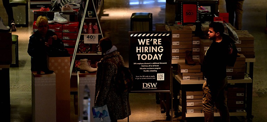 Sign reading “WE’RE HIRING TODAY” sits beside shoppers at the King of Prussia Mall in December, 2022.