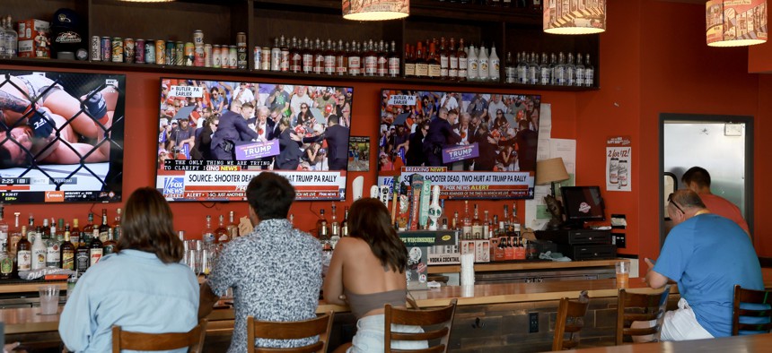 People watch a news station broadcast of the scene as former U.S. President Donald Trump is rushed off stage by Secret Service at his Pennsylvania rally, at a bar across the street from the Fiserv Forum where the Republican National Convention will be held, on July 13, 2024, in Milwaukee, Wisconsin.